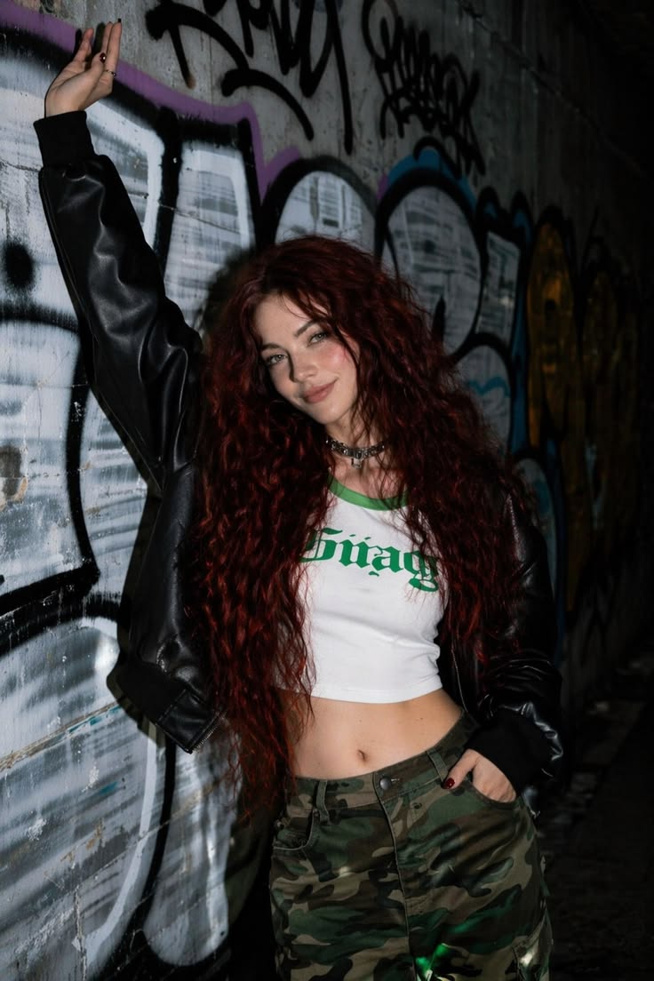 Red-haired woman in streetwear posing against a graffiti-covered wall, created with AI image generation.